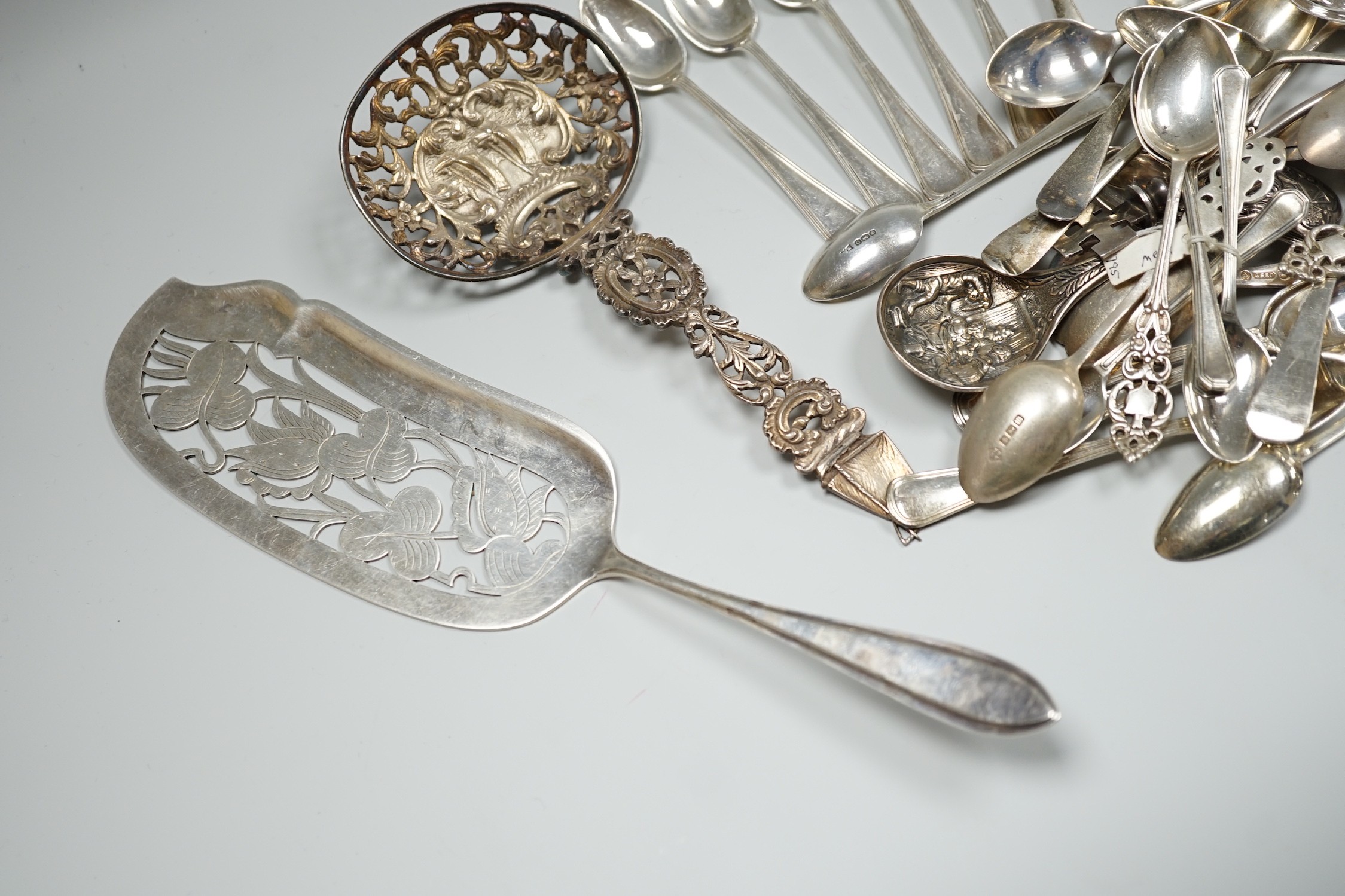 A group of mixed silver and white metal items including flatware, Dutch fish slice, German 800 tea strainer, George IV 'Claret' wine label, etc. and a plated spoon.